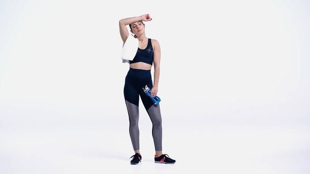 tired sportswoman with towel and sports bottle standing on white - Photo, Image