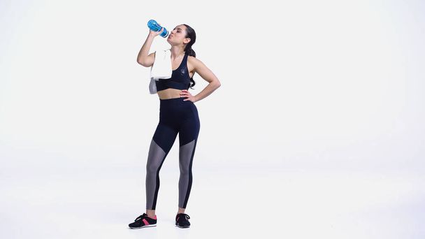 молодая спортсменка с полотенцем питьевой воды из спортивной бутылки на белом - Фото, изображение