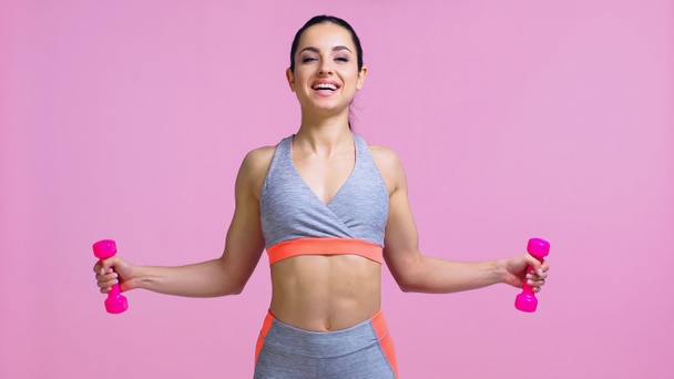 positive sportswoman working out with dumbbells isolated on pink - Zdjęcie, obraz