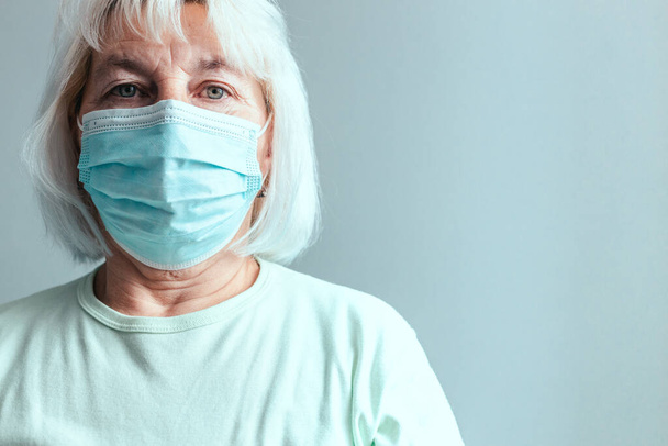 Portrait of Caucasian woman in a medical mask isolated on a grey wall background. - Foto, imagen