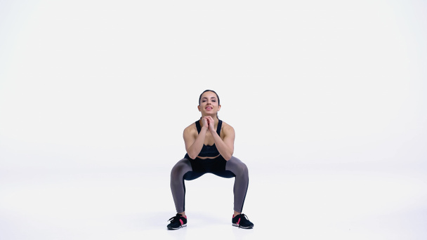 full length of young and happy sportswoman doing squat exercise on white - Valokuva, kuva
