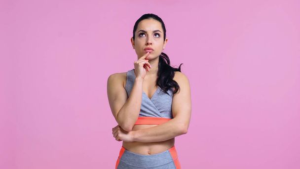 thoughtful young woman in sportswear looking away isolated on pink - Фото, изображение