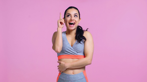 amazed young woman in sportswear pointing with finger and looking up isolated on pink - Фото, изображение