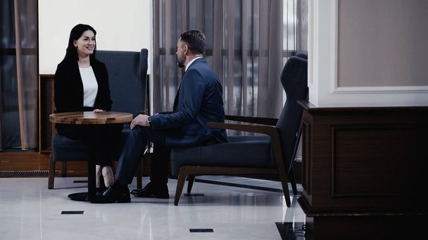 businessman and cheerful businesswoman sitting in lobby of restaurant during business meeting  - Foto, Imagen