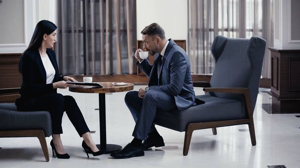 Businessman drinking coffee during business meeting with woman in restaurant lobby - Zdjęcie, obraz