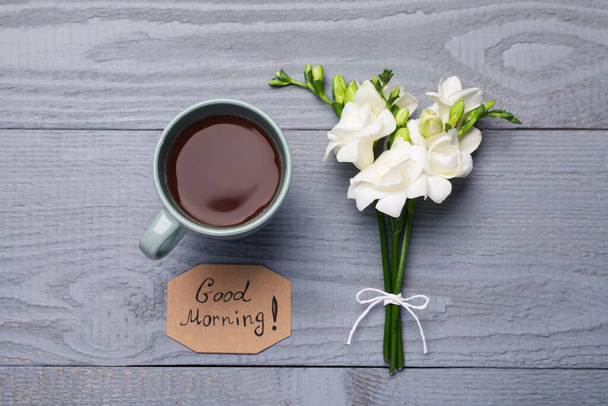 Fresh tea, flowers and Good Morning! message on grey wooden table, flat lay - Fotoğraf, Görsel