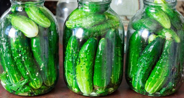 Yeşil salatalıkların korunması. Masada salatalık ve baharatlı şeffaf cam kavanozlar var. Koruma süreci, kış hazırlıkları - Fotoğraf, Görsel