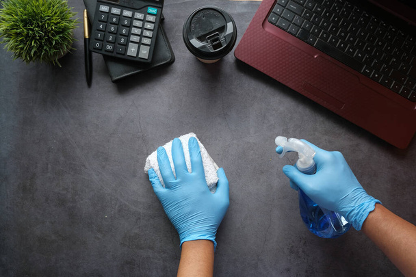 hand in blue rubber gloves holding spray bottle cleaning office table  - Photo, Image