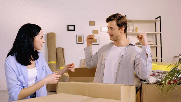 happy woman looking at boyfriend showing muscles near carton boxes - Photo, Image