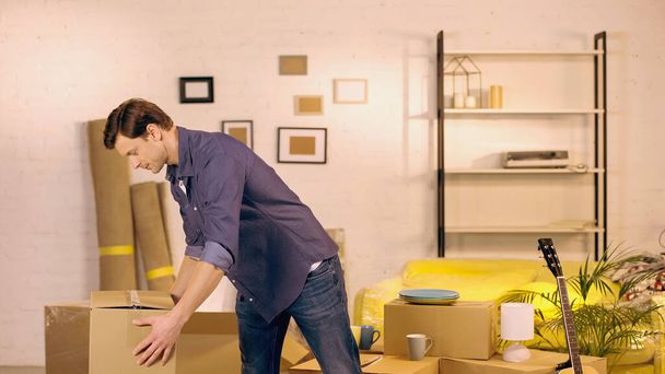 Young man putting cardboard box in new home - Photo, Image