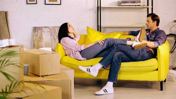 mężczyzna i kobieta spoczywający na kanapie w pobliżu pudełek kartonowych  - Zdjęcie, obraz