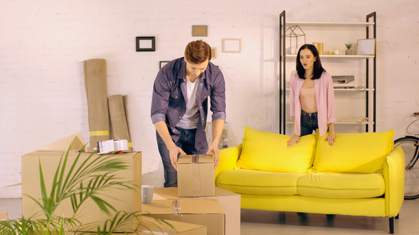 woman talking while looking at boyfriend unpacking box in new home - Foto, afbeelding