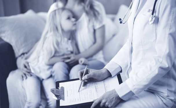 Doctor and patient. Pediatrician using clipboard while examining little girl with her mother at home. Sick and unhappy child at medical exam. Medicine concept - Fotografie, Obrázek