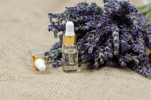 Natural lavender oil. Bottles with lavender oil and a fresh bouquet of lavender on a burlap background - Photo, Image
