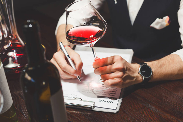 Sommelier writes on clipboard describing red wine at table - Zdjęcie, obraz