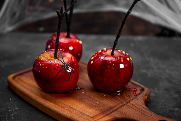 Red apples in caramel with a festive Halloween decor, an original treat for a festive Halloween table decorated with spiders and cobwebs - Foto, afbeelding