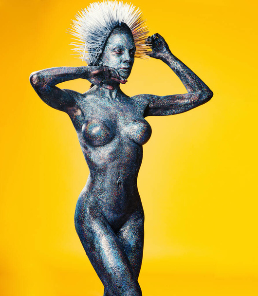 girl with mohawk and athletic figure covered in glitter on yellow background - Fotó, kép