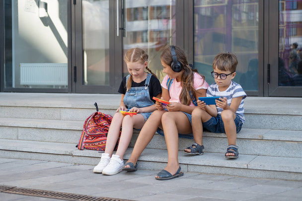  Tres niños con mochila sentarse y jugar popit y teléfono - Foto, Imagen