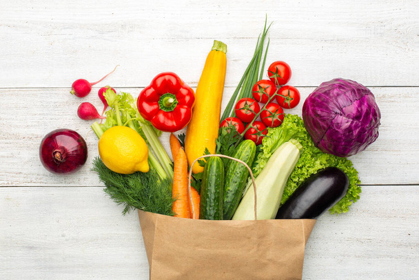 Vegetables in a paper bag on a white wooden background. Shopping in a supermarket or market. - Fotografie, Obrázek