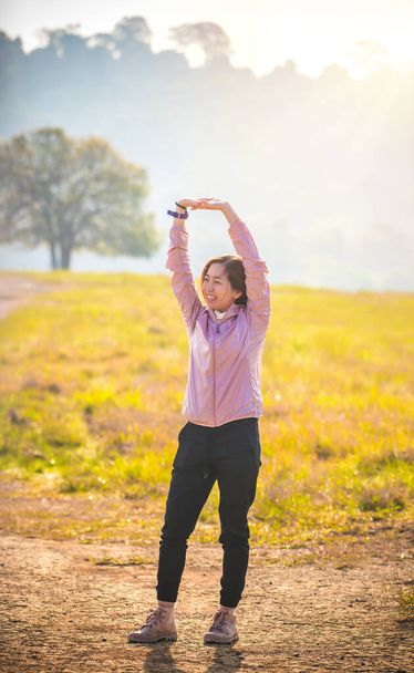Mujer joven con ropa de entrenamiento. Ella está estirando sus brazos listos para hacer ejercicio por la mañana. Mujer joven calentando al aire libre. sol día. - Foto, imagen
