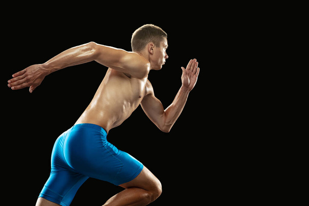 Young professional male athlete, runner training isolated on dark studio background. Muscular, sportive man. Concept of sport, healthy lifestyle - Foto, afbeelding