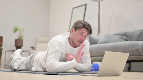 Hombre de mediana edad hablando en videollamada en la estera del yoga del ordenador portátil en casa - Foto, imagen