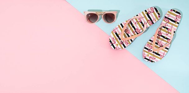 Летние сандалии, флип-флоп и розовые солнцезащитные очки на розовом и голубом фоне, вид сверху, пространство для копирования - Фото, изображение