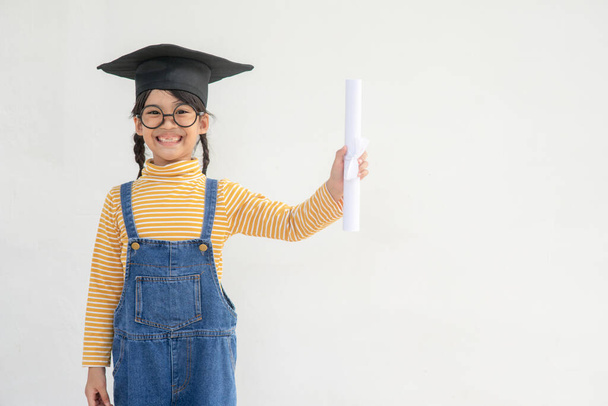Азиатская маленькая девочка в шапке выпускника и с дипломом на белом фоне - Фото, изображение