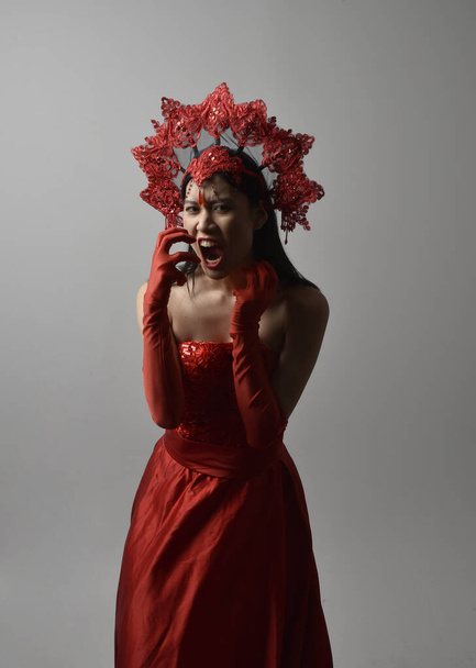 Close-up portret van mooie jonge Aziatische vrouw met rood korset, lange operahandschoenen en sierlijke kroonhoofdtooi. Gestural hand poses geïsoleerd op licht studio achtergrond. - Foto, afbeelding