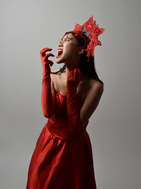 Nahaufnahme Porträt der schönen jungen asiatischen Frau mit rotem Korsett, langen Opernhandschuhen und kunstvoller Kopfbedeckung. Gestenreiche Hand posiert isoliert auf hellem Studiohintergrund. - Foto, Bild