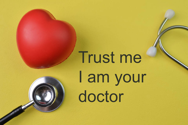 Stethoscope and heart shape on yellow background with phrase TRUST ME I AM YOUR DOCTOR - Foto, Imagen