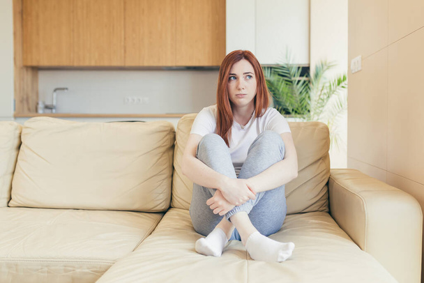 Young beautiful woman sitting alone at home on the couch, feeling pain and depression - Foto, Imagen