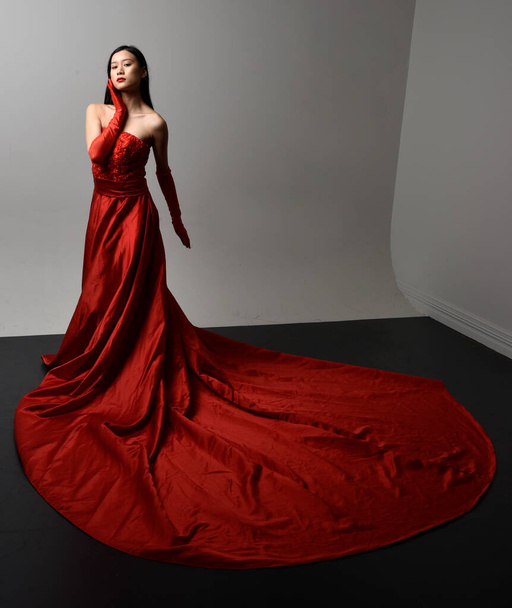 Teljes hosszúságú portré gyönyörű fiatal ázsiai nőről piros fűzővel, hosszú operakesztyűvel és díszes fejdísszel. Geszturális kéz pózol elszigetelt fény stúdió háttér. - Fotó, kép
