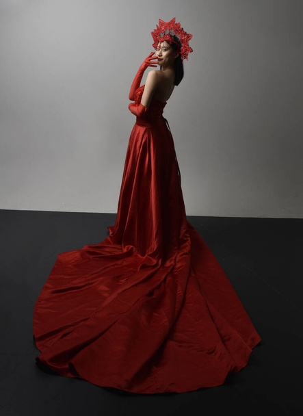 Portrait complet de belle jeune femme asiatique portant un corset rouge, de longs gants d'opéra et une coiffe de couronne ornée. La main gestuelle pose isolée sur fond de studio lumineux. - Photo, image