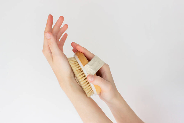 Hand is holding hatural wooden body brush in front of white background. Woman scrubbing her hand. Massage, relax, spa. eco-friendly, zero waste product. Beauty, skincare, wellness concept - Фото, изображение