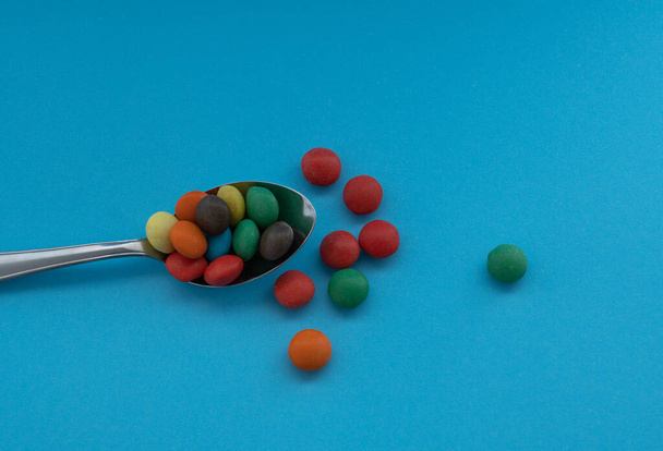 close-up of a spoon with colored chocolate sprinkles. a blue background is observed. the view of the photograph is from above - Foto, Imagem
