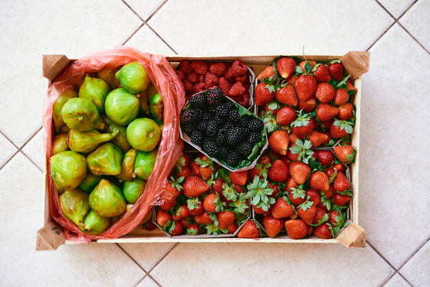 Kit de madera con cajas de fresas, frambuesas, higos y moras se encuentra en una baldosa ligera - Foto, imagen