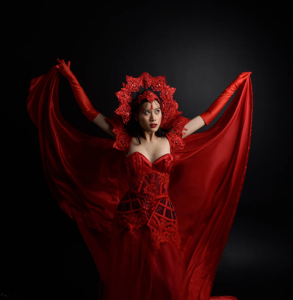 portrait of beautiful young asian woman wearing red corset, long opera gloves and ornate crown headdress. Sitting pose with gestural hands  isolated on light studio background. - Foto, immagini
