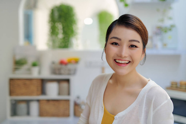 Portrait of young smiling woman sitting against home kitchen background - Photo, image