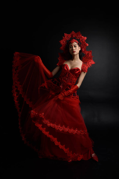 Full length  portrait of beautiful young asian woman wearing red corset, long opera gloves and ornate crown headdress. Graceful posing  isolated on light studio background. - Foto, imagen