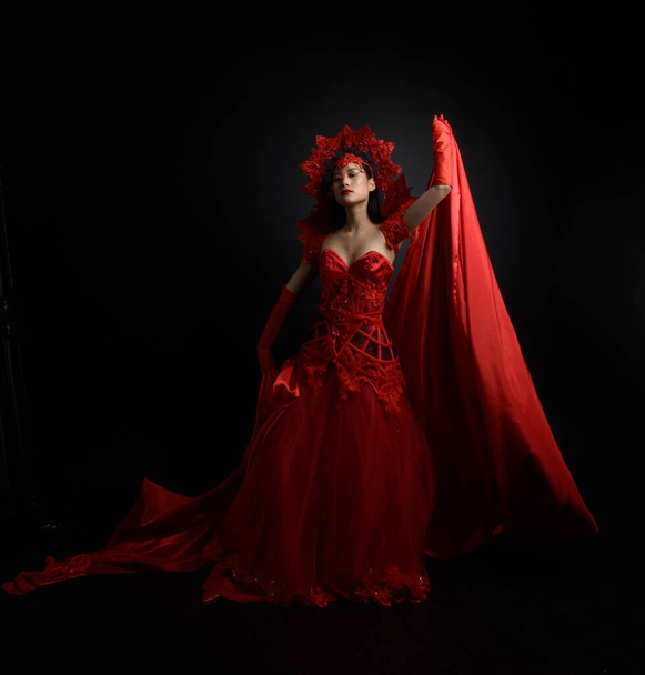 Full length  portrait of beautiful young asian woman wearing red corset, long opera gloves and ornate crown headdress. Graceful posing  isolated on light studio background. - Fotografie, Obrázek