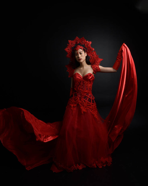 Full length  portrait of beautiful young asian woman wearing red corset, long opera gloves and ornate crown headdress. Graceful posing  isolated on light studio background. - Foto, Imagem