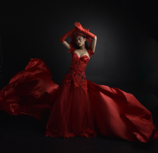 Portret pięknej młodej Azjatki w czerwonym gorsecie, długich rękawiczkach operowych i ozdobnym nakryciu głowy korony. Graceful pozowanie izolowane na tle światła studio. - Zdjęcie, obraz