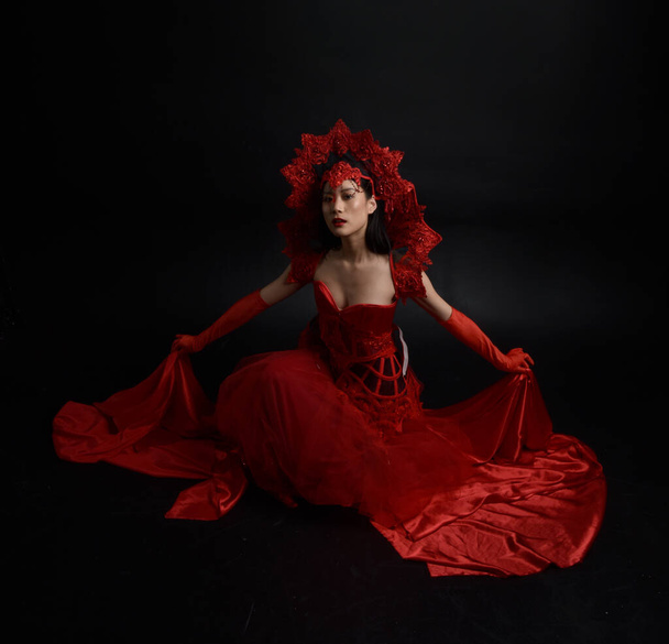 Full length  portrait of beautiful young asian woman wearing red corset, long opera gloves and ornate crown headdress. Graceful posing  isolated on light studio background. - Foto, Imagen