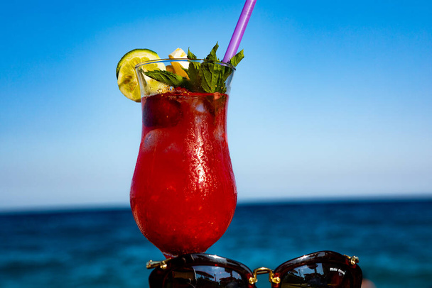 Roter Cocktail mit Sonnenbrille am Strand auf einem Holztisch - Foto, Bild