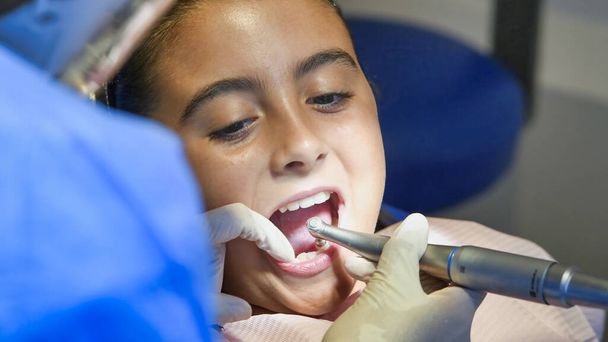 Fiatal fehér nő, fehér latex kesztyűs fogorvossal, ellenőrizze a fogai állapotát. csecsemő lány kék fogorvosi székben - Fotó, kép