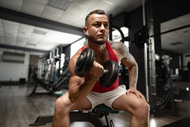 Portrait of man bodybuilder in red shirt in gym - Фото, изображение
