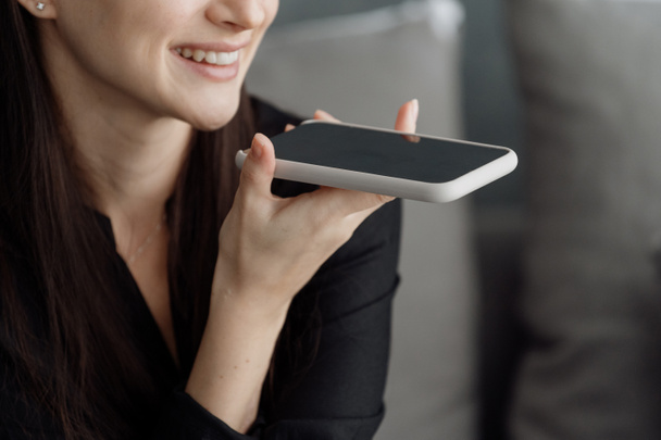 Περικοπή shot χαρούμενη γυναίκα χρησιμοποιώντας ηχείο του σύγχρονου ηχείου smartphone, ενώ μιλάμε με φίλο ή την οικογένεια, χαλαρώνοντας στον καναπέ στο σπίτι, χαμογελώντας θηλυκό φωνητικό μήνυμα εγγραφής στο gadget - Φωτογραφία, εικόνα