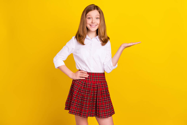 Photo of nice blond teenager girl hold empty space wear white shirt skirt isolated on yellow color background - Fotó, kép