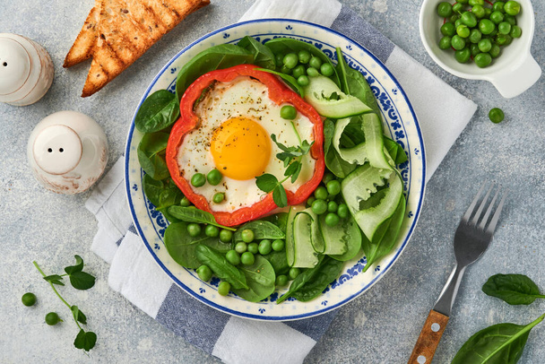 Red bell peppers stuffed with eggs, spinach leaves, green peas and microgreens on a breakfast plate on light grey table background. Top view. - Zdjęcie, obraz